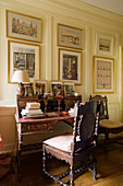 Antique bureau and wooden chair below gallery of pictures on yellow wall