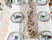 Weihnachtlich gedeckter Tisch mit Tischläufer, Zapfen und geometrischen Dekoobjekten