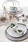 Weihnachtlich gedeckter Tisch mit Serviettendeko, Zapfen und geometrischem Dekoobjekt