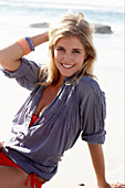 A blonde woman on a beach wearing a red bikini and a blue blouse