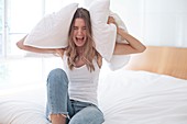 Young woman holding pillow over her ears and screaming