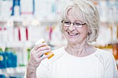 Senior woman reading pill bottle label in pharmacy