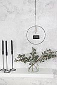 DIY wall decoration: metal ring with motto above vase of eucalyptus branches and black candles