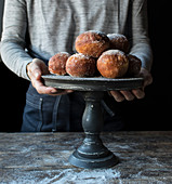Crop human holding tray with set of fresh beignets with powdered sugar