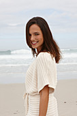 A brunette woman by the sea wearing a short-sleeved cardigan