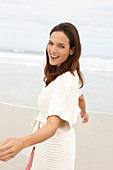 A brunette woman by the sea wearing a short-sleeved cardigan