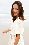 A brunette woman by the sea wearing a short-sleeved cardigan