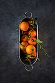 Mandarins with leaves in a tin containers on a grey surface