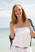 A young woman on a beach wearing a white summer dress and a striped cardigan