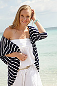 A young woman on a beach wearing a white summer dress and a striped cardigan