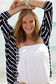 A young woman on a beach wearing a white summer dress and a striped cardigan