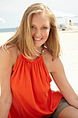 A blonde woman on a beach wearing an orange top