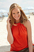 A blonde woman on a beach wearing an orange top