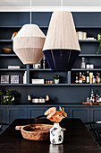 Threaded lampshades above the dining table in front of the shelf wall