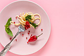 Spaghetti with tomato and pesto sauce on pink background