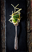 Spaghetti mit Pesto auf Gabel vor dunklem Hintergrund