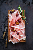 Prosciutto ham with olives on wooden cutting board