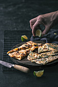 Hand putting pieces of fresh lime on board with slices of tasty gozleme near knife and grating