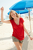 A blonde woman on a beach wearing a red top and shorts