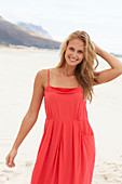 Junge blonde Frau in rotem Sommerkleid am Strand