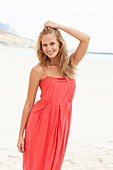 Junge blonde Frau in rotem Sommerkleid am Strand