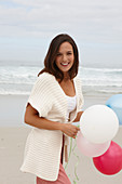 A brunette woman wearing a short-sleeved cardigan and holding balloons