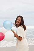 A brunette woman wearing a short-sleeved cardigan and holding balloons