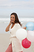 A brunette woman wearing a short-sleeved cardigan and holding a balloon