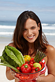 Junge brünette Frau mit Gemüseschale am Strand