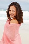 A brunette woman by the sea with a pink shawl