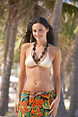 A young brunette woman wearing a necklace, a silver bikini top and a beach towel