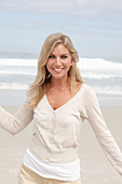 A blond woman on a beach wearing a light cardigan and shorts