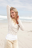 A blond woman on a beach wearing a light cardigan and shorts