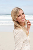 A blond woman on a beach wearing a light cardigan