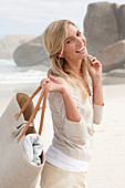 Blonde Frau mit Tasche in hellem Cardigan und Shorts am Strand