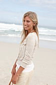 A blond woman on a beach wearing a light cardigan and shorts