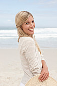 A blond woman on a beach wearing a light cardigan