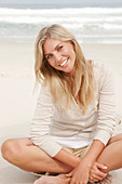 Blonde Frau in hellem Cardigan und Shorts am Strand