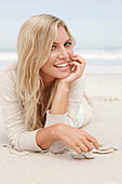 A blond woman on a beach wearing a light cardigan