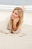 A blond woman on a beach wearing a light cardigan and shorts