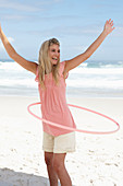 Junge Frau mit Hula-Hoop-Reifen im rosa Top und Shorts am Strand