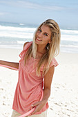 A young woman on a beach with a hula-hoop wearing a pink top and shorts