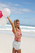 Junge Frau mit Luftballons im rosa Top und Jeansshorts am Strand