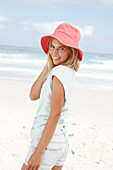 A blonde woman on the beach wearing a light t-shirt and a red hat