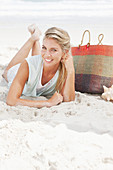 A blonde woman lying on the beach wearing a light t-shirt