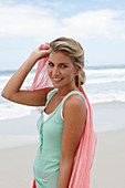 A blonde woman on a beach with a scarf and a turquoise top