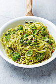 Spaghetti with spinach pesto, toasted pine nuts and basil leaves in a pan