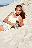 A brunette woman on a beach with a bottle of water wearing a light top and shorts