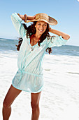 Brünette Frau mit Hut in hellblauem Strandkleid am Meer