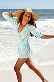 Brünette Frau mit Hut in hellblauem Strandkleid am Meer